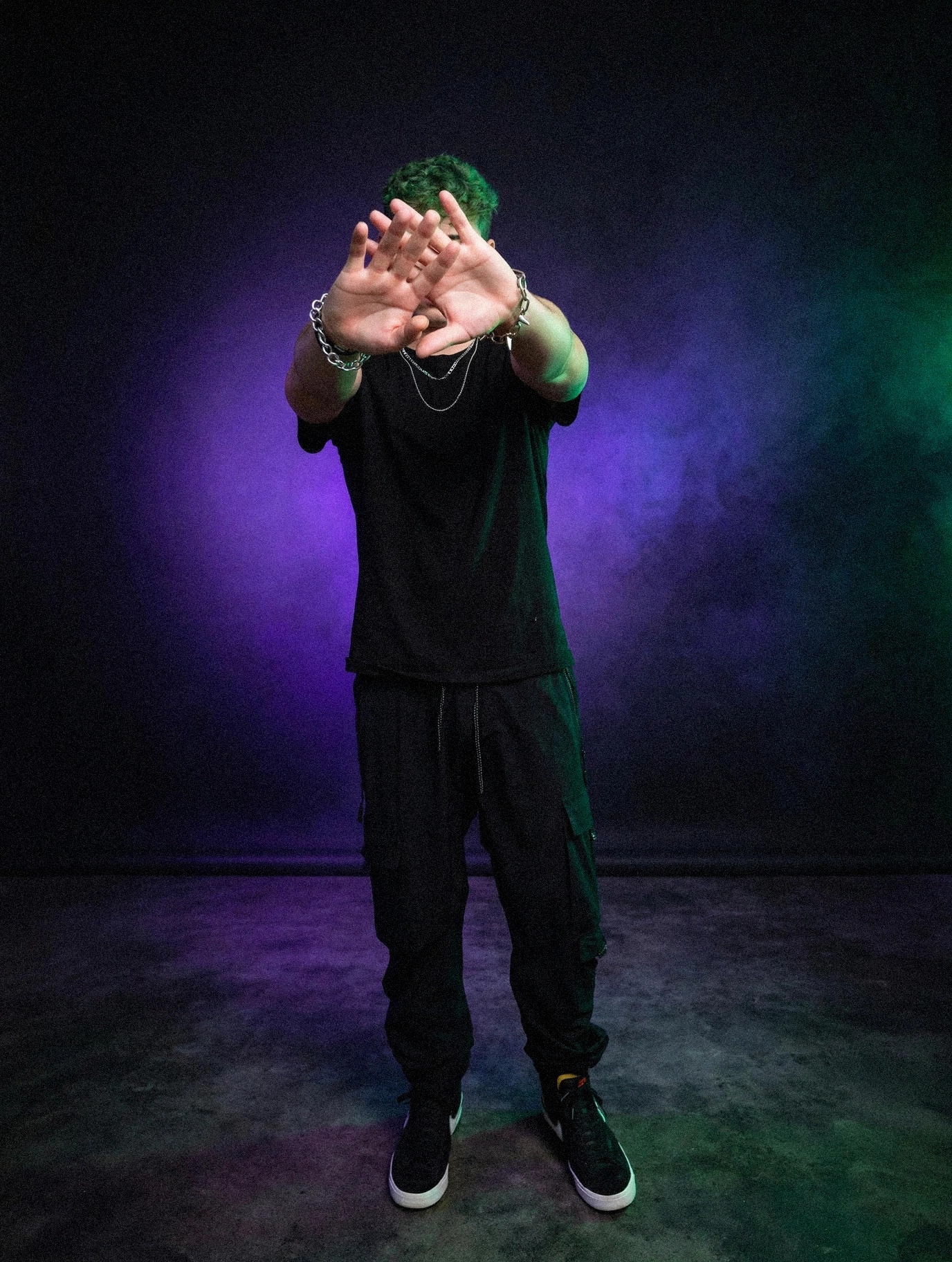 Mellow777 with hands raised before a purple and green studio backdrop