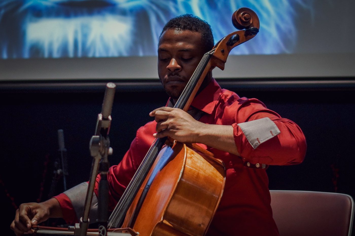 RAHAM playing cello on stage in a red shirt