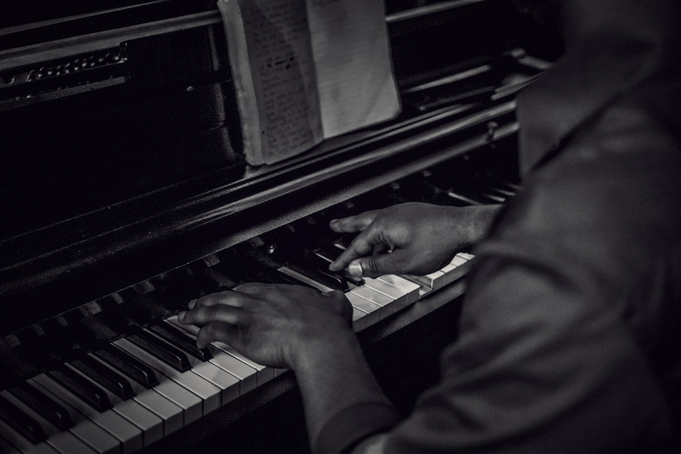 Hands on piano keys beside sheet music, in black and white