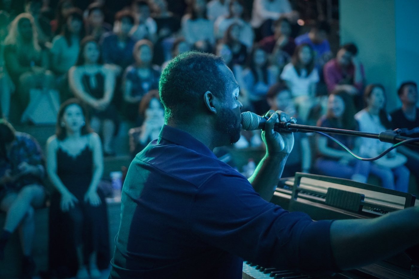 RAHAM singing into a microphone at the keyboard before a crowd