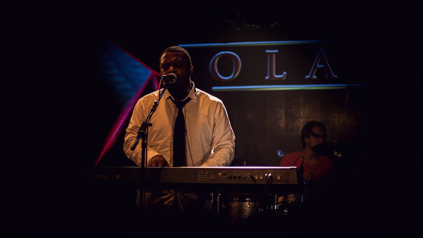 RAHAM on keyboards on stage with the OLAM sign behind him